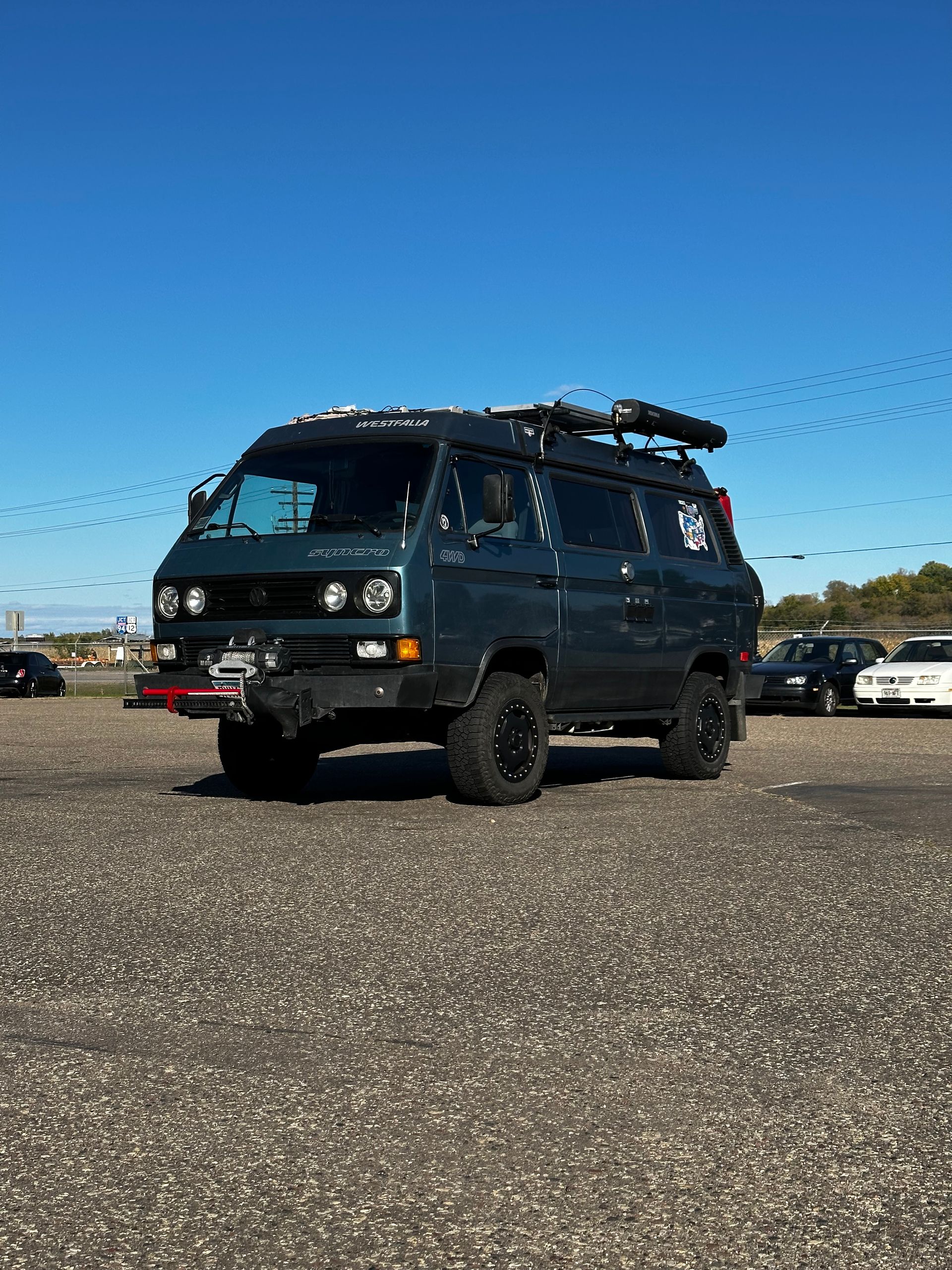 A van with a surfboard on top of it is parked in a gravel lot