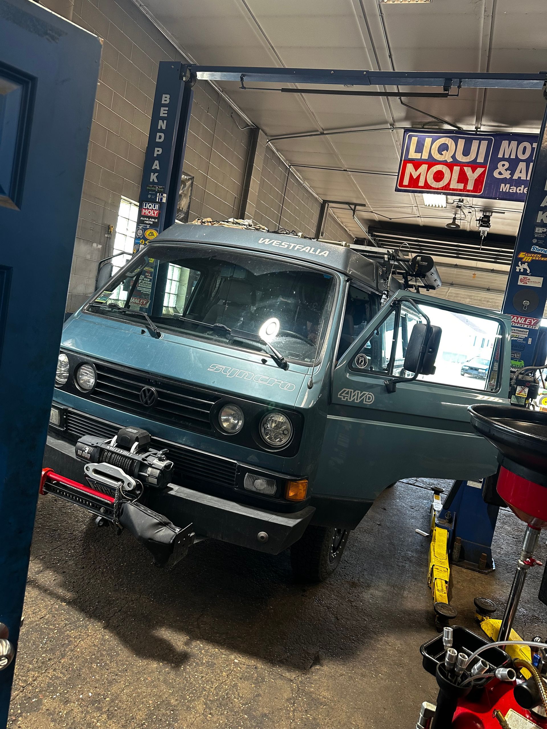 A blue van is parked in a garage with its doors open