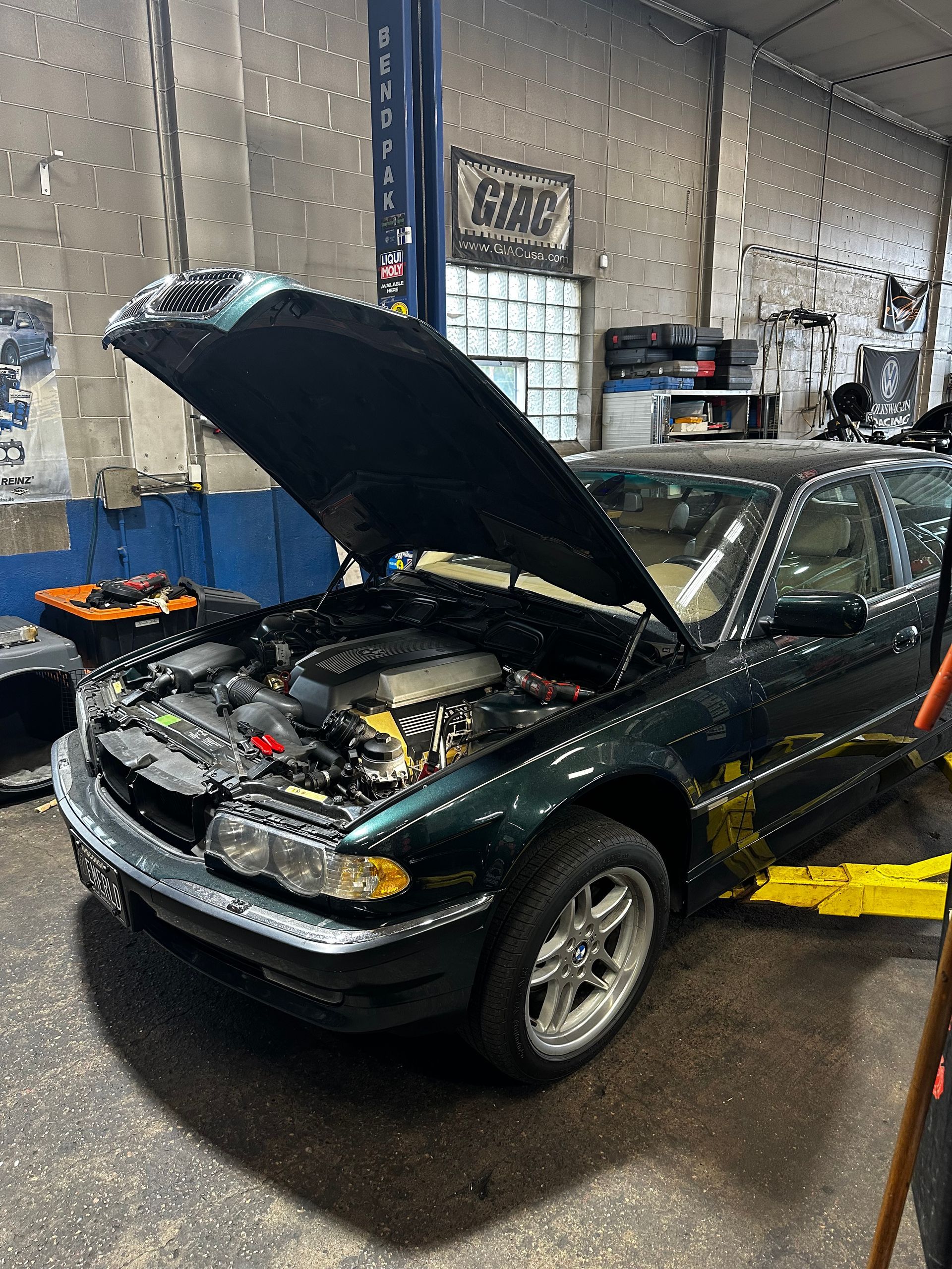 A green car with the hood up is on a lift in a garage
