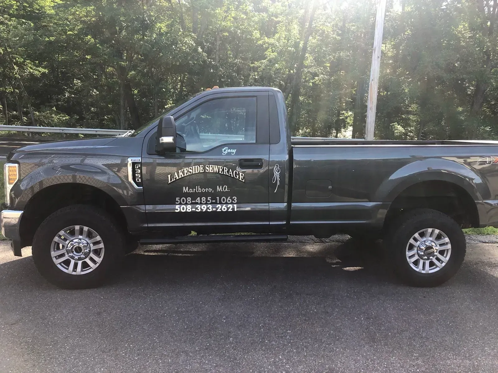 Dark gray pickup truck with business name and phone number on the side, parked on asphalt.