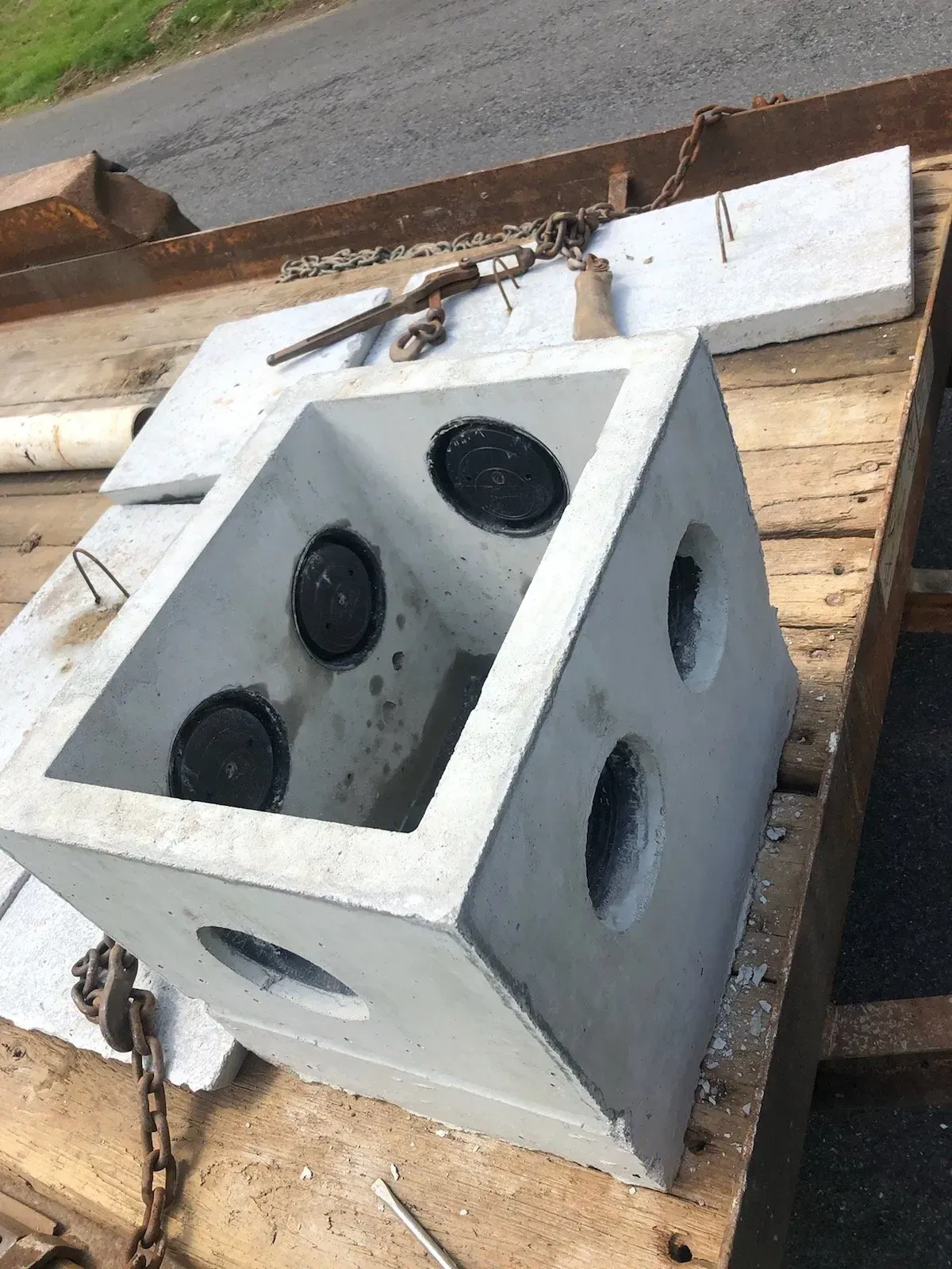 Concrete utility box with four circular openings, sitting on a trailer, next to concrete lids.