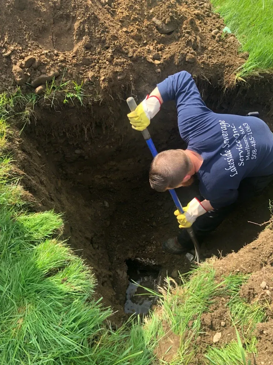 Person digging in a hole in the ground with a shovel, surrounded by grass.