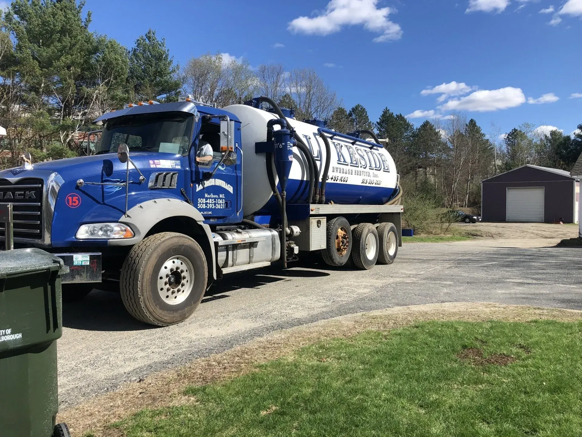 Blue septic service truck on a gravel driveway in front of a garage, sunny day.