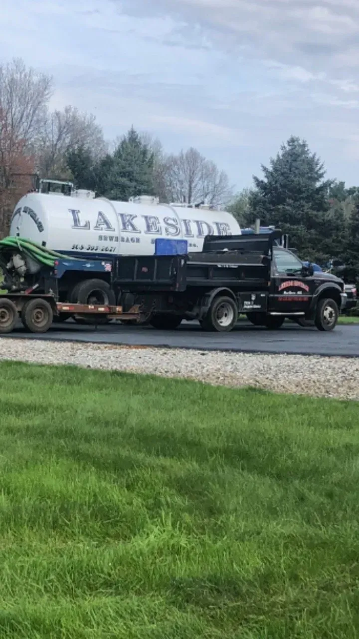 A Lakeside Services truck towing a tanker and a dump truck, parked on asphalt.