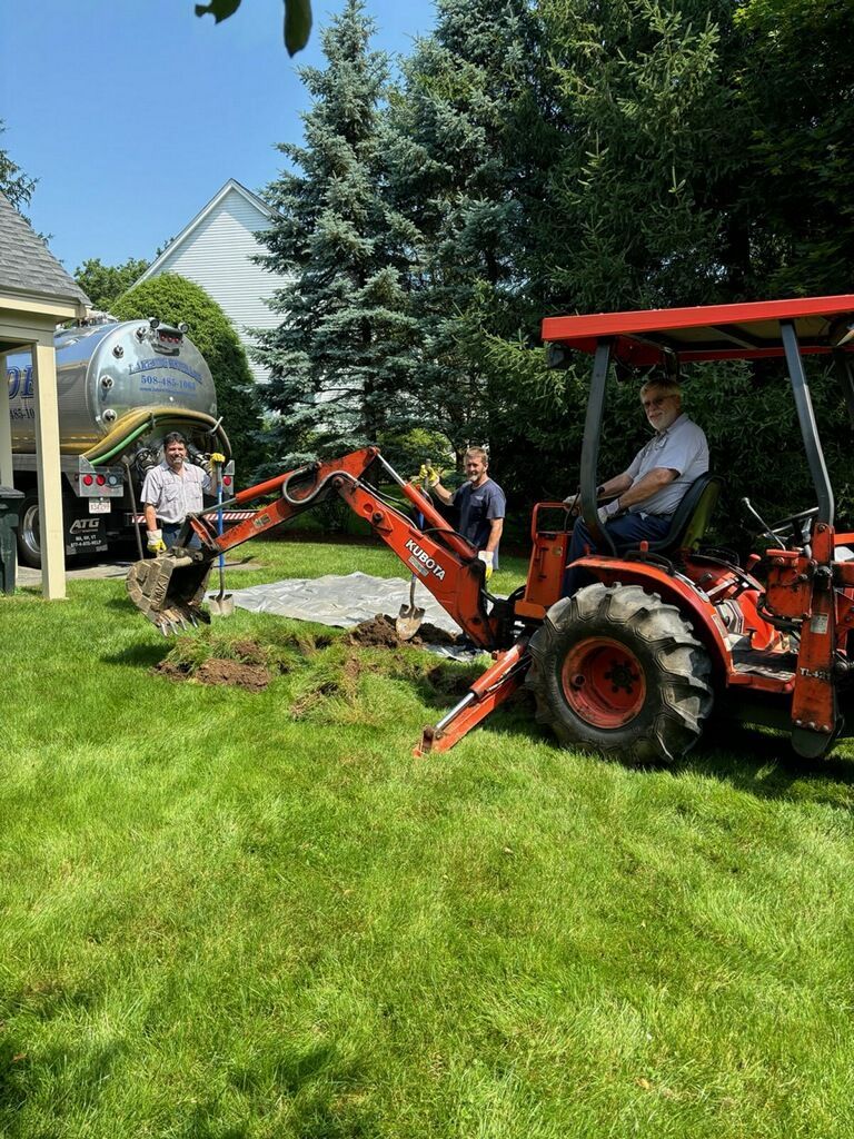 Men working on a lawn with a tractor and a tanker truck in a yard on a sunny day.