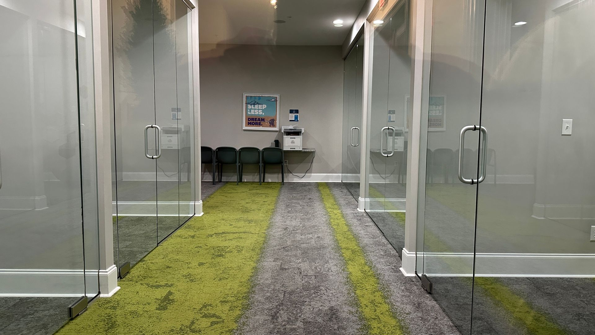 Hallway with glass-walled offices, green-striped carpet, and a waiting area with chairs.