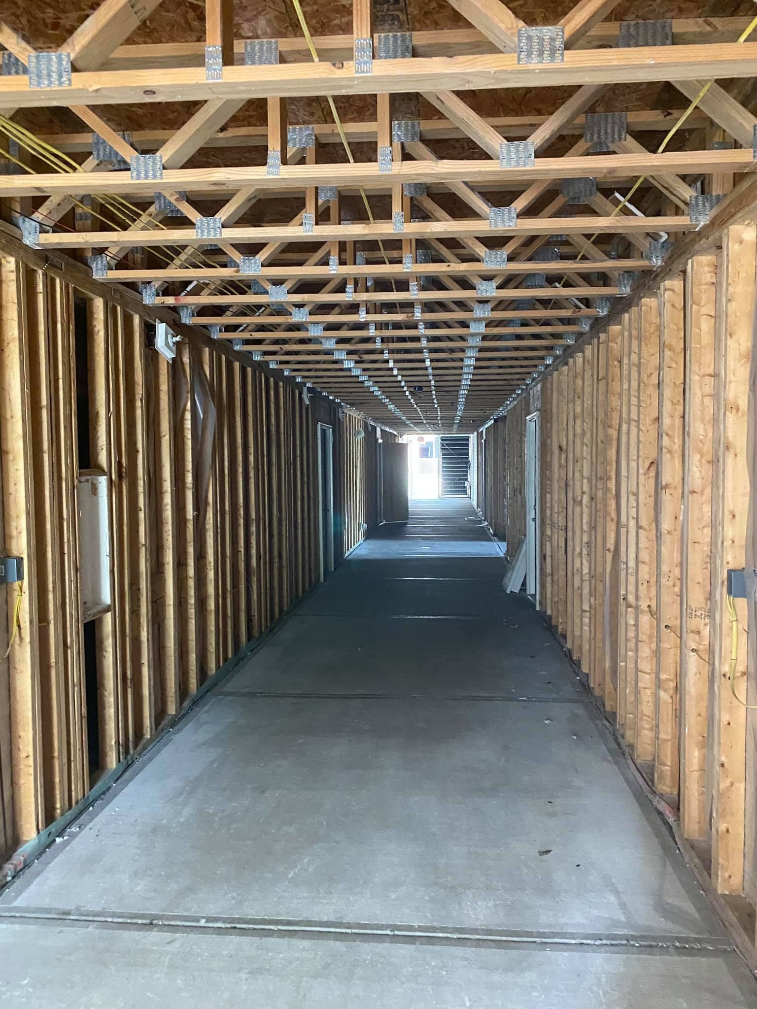Long hallway under construction, wood framing, concrete floor, exposed trusses.