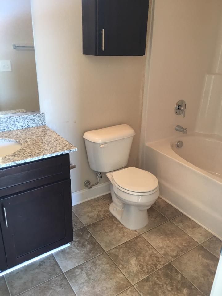 Bathroom with a toilet, tub, vanity, and dark cabinets; tile floor, neutral walls.