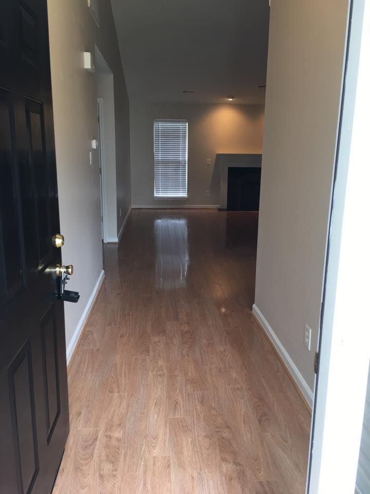 Open front door revealing a hallway with wood-look floors leading to a living area with a fireplace.