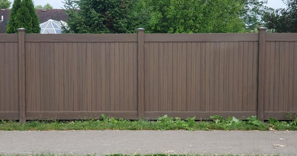 A brown wooden fence is sitting next to a sidewalk.
