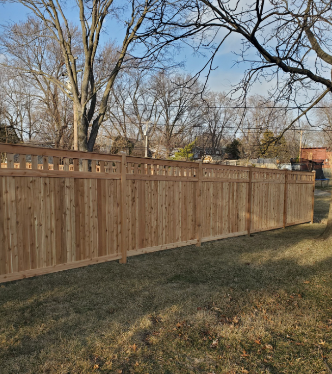 A wooden fence is surrounded by grass and trees in a yard.