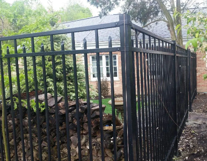 A black metal fence is surrounding a brick house.