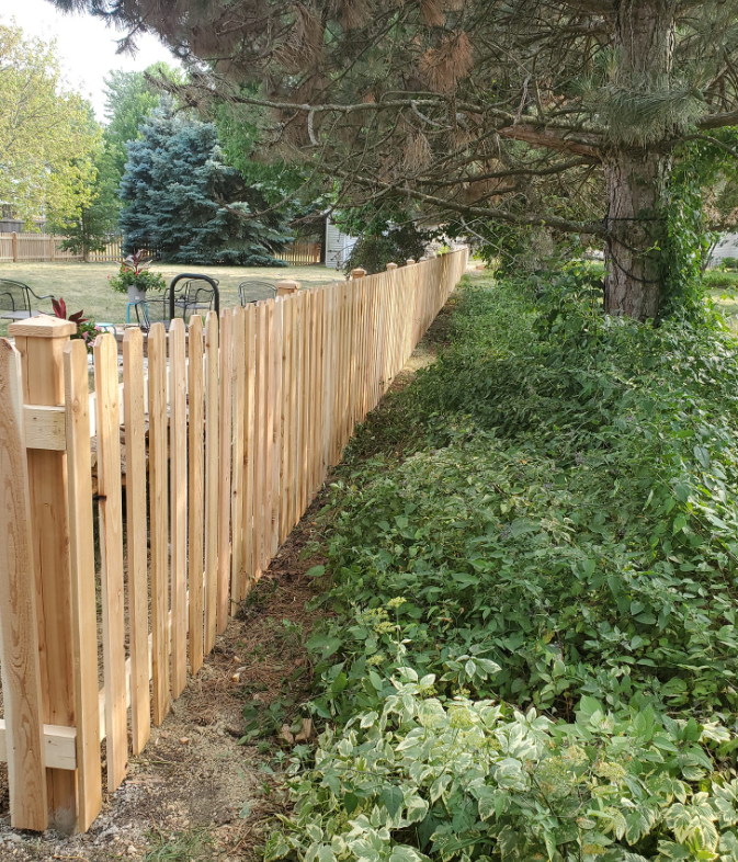 A wooden picket fence is surrounded by trees and bushes.