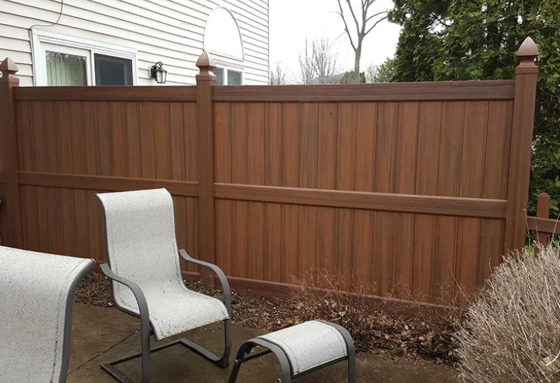 A wooden fence with chairs and ottomans in front of it