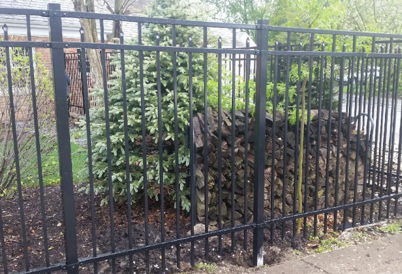 A black metal fence surrounds a pile of wood.