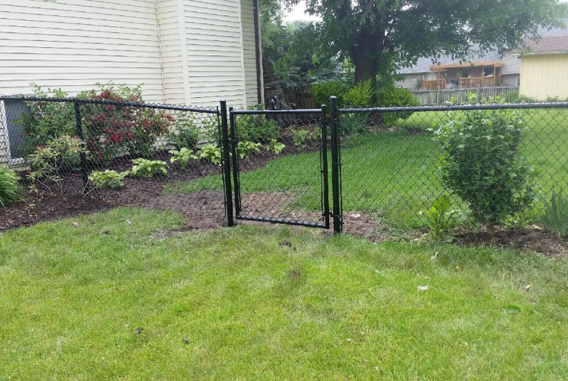 A chain link fence with a gate in the backyard of a house.