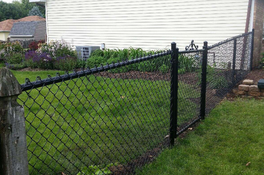 A black chain link fence is in the backyard of a house.