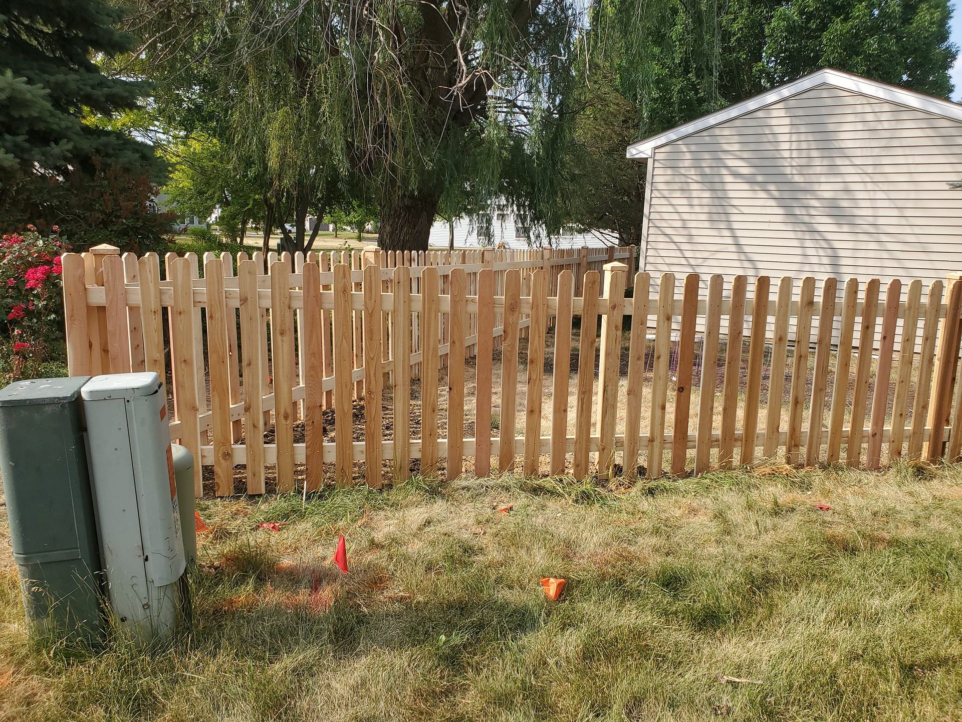 A wooden picket fence in a yard next to a shed.
