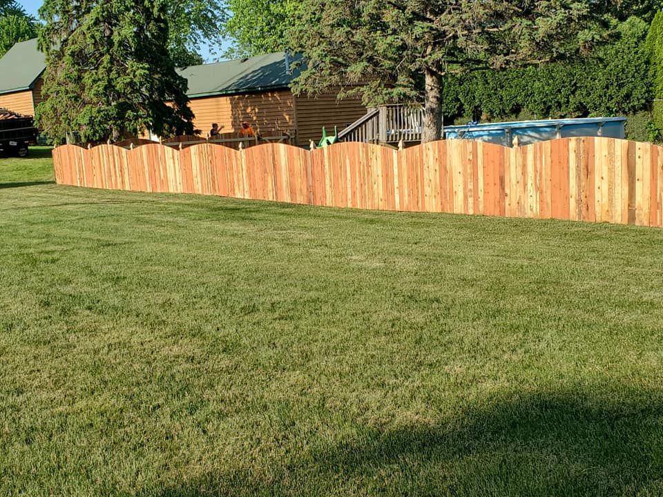 A wooden fence surrounds a lush green lawn in front of a house.