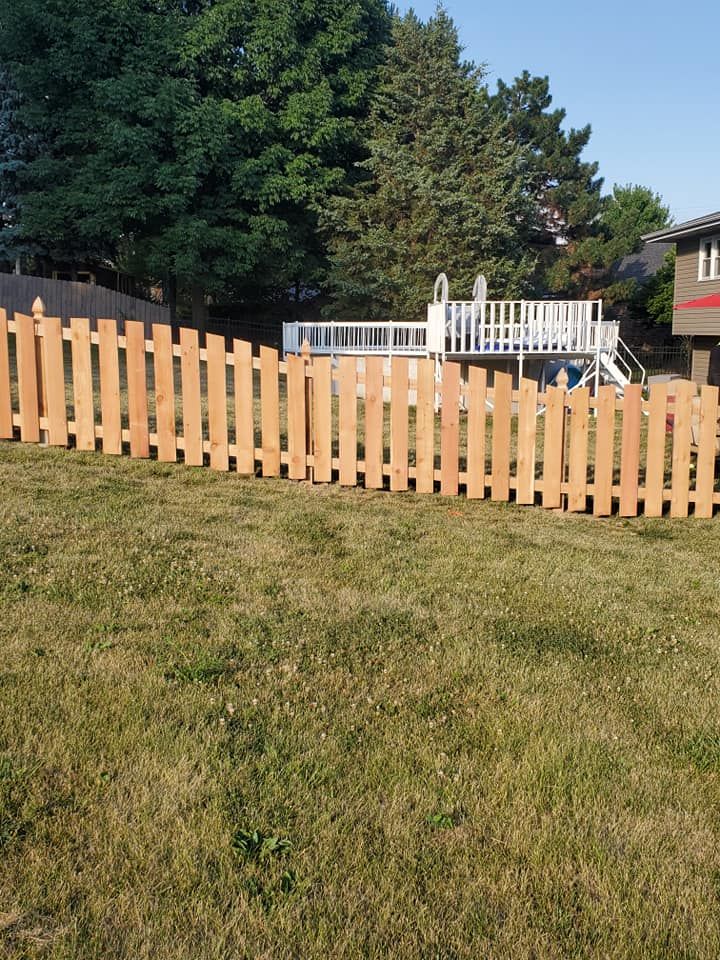 A wooden picket fence surrounds a lush green field in front of a house.