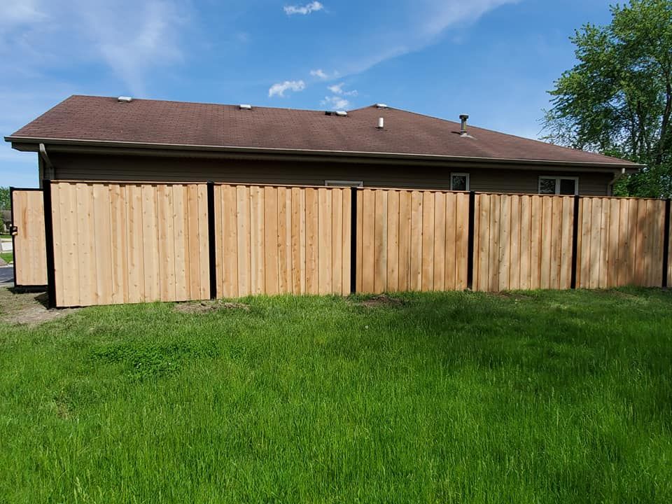 A wooden fence is surrounding a house in a grassy yard.