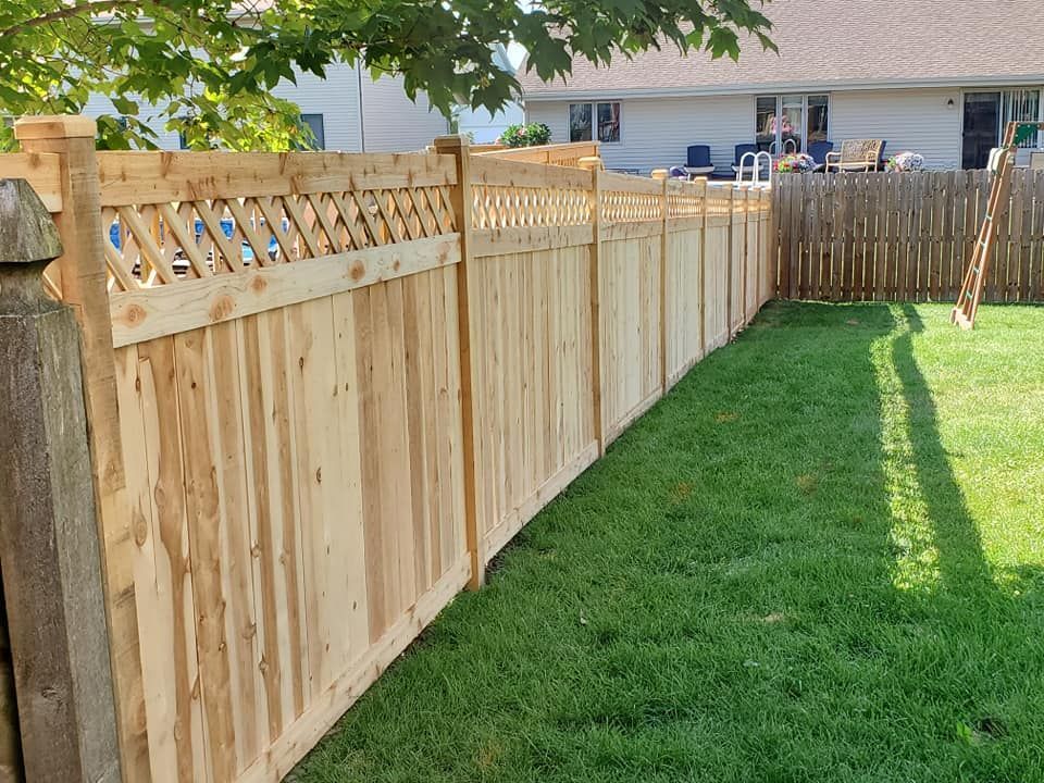 A wooden fence surrounds a lush green yard in front of a house.