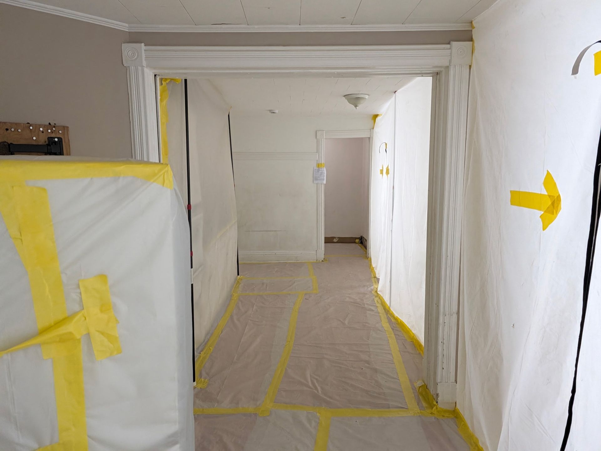 Hallway under renovation, with taped-off walls and floor covered in protective paper.