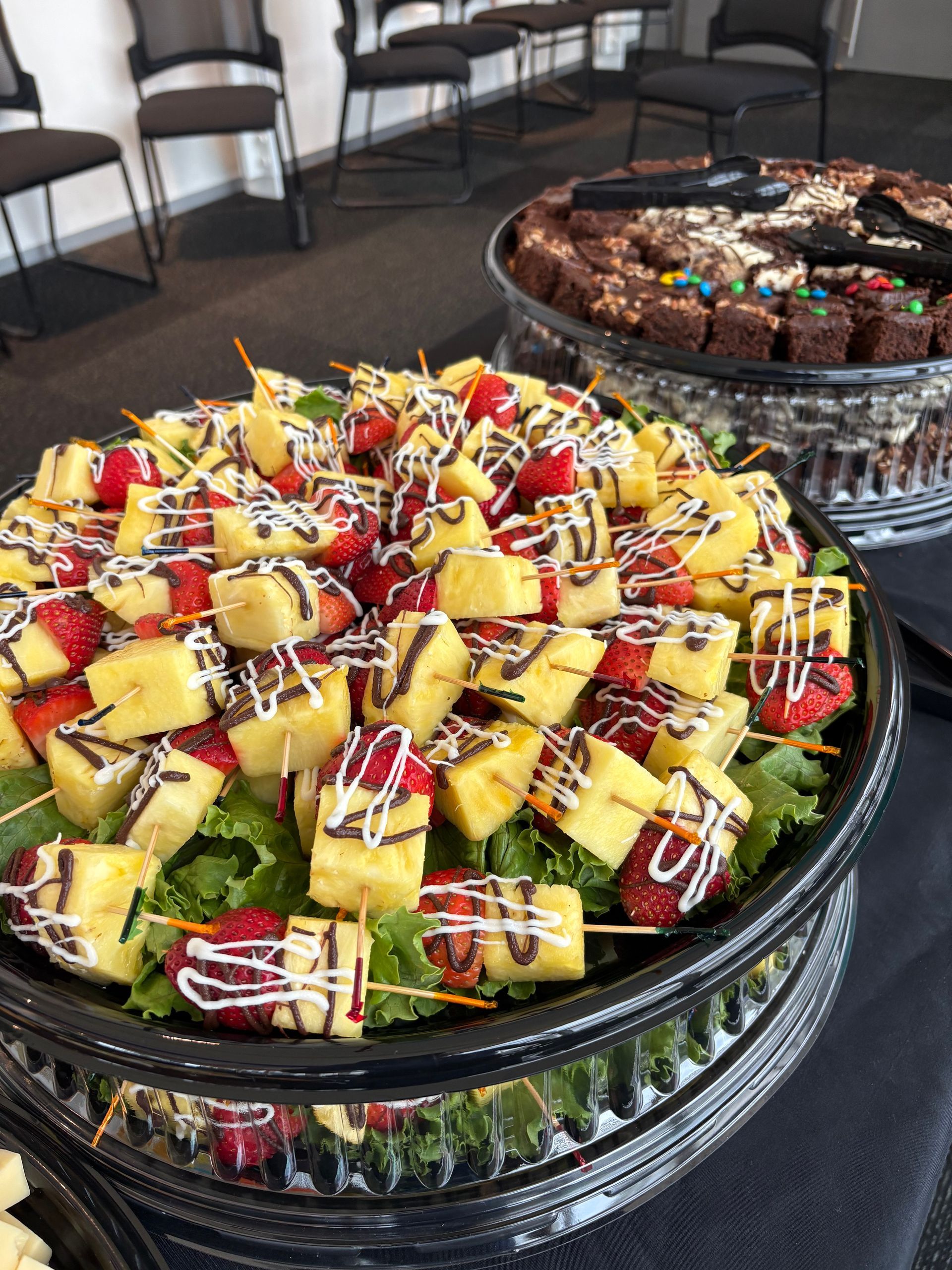 Fruit skewers with pineapple and strawberries drizzled with chocolate, and brownies.