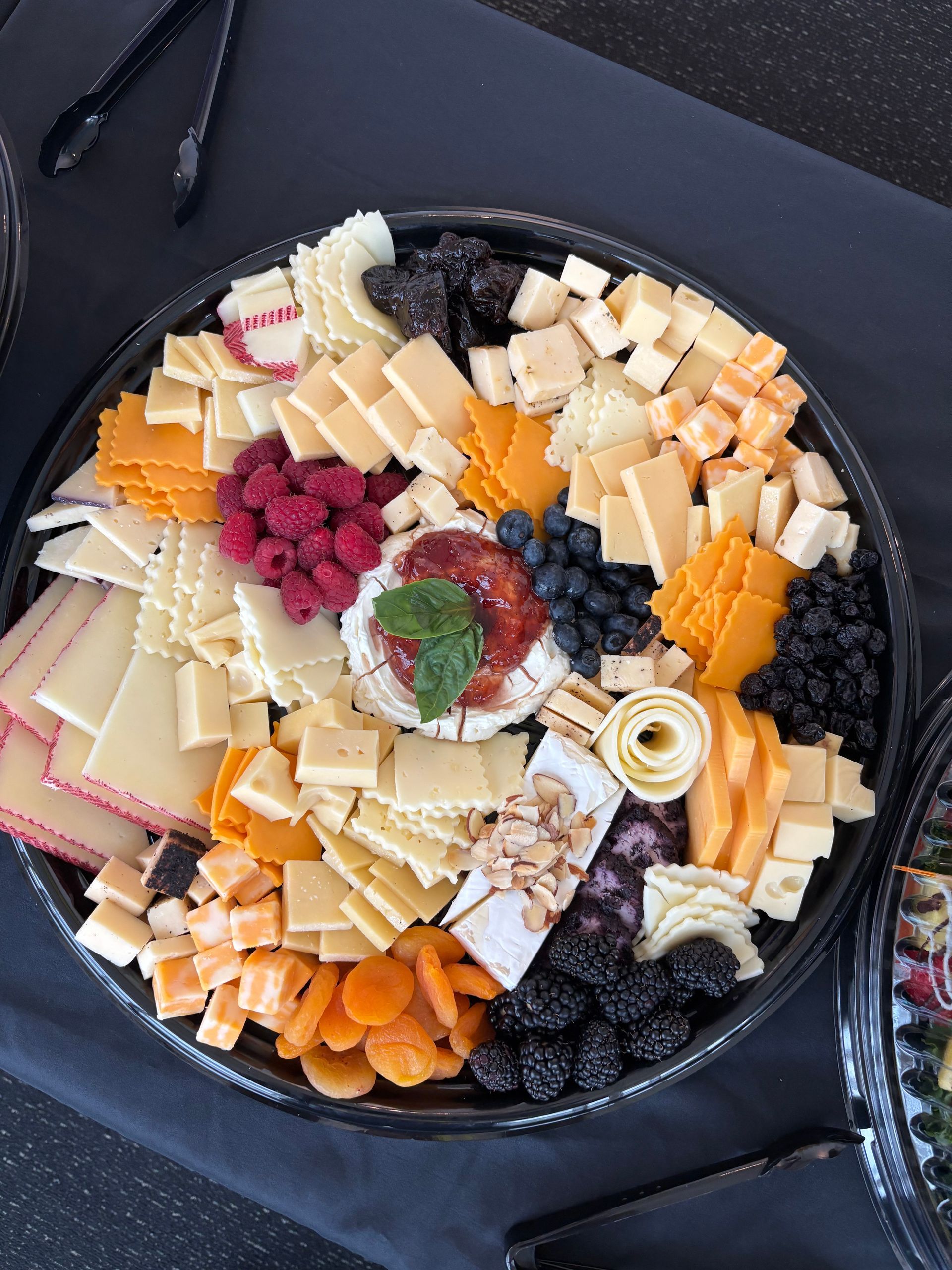 Cheese and fruit platter with various cheeses, berries, and dried apricots on a black tray.