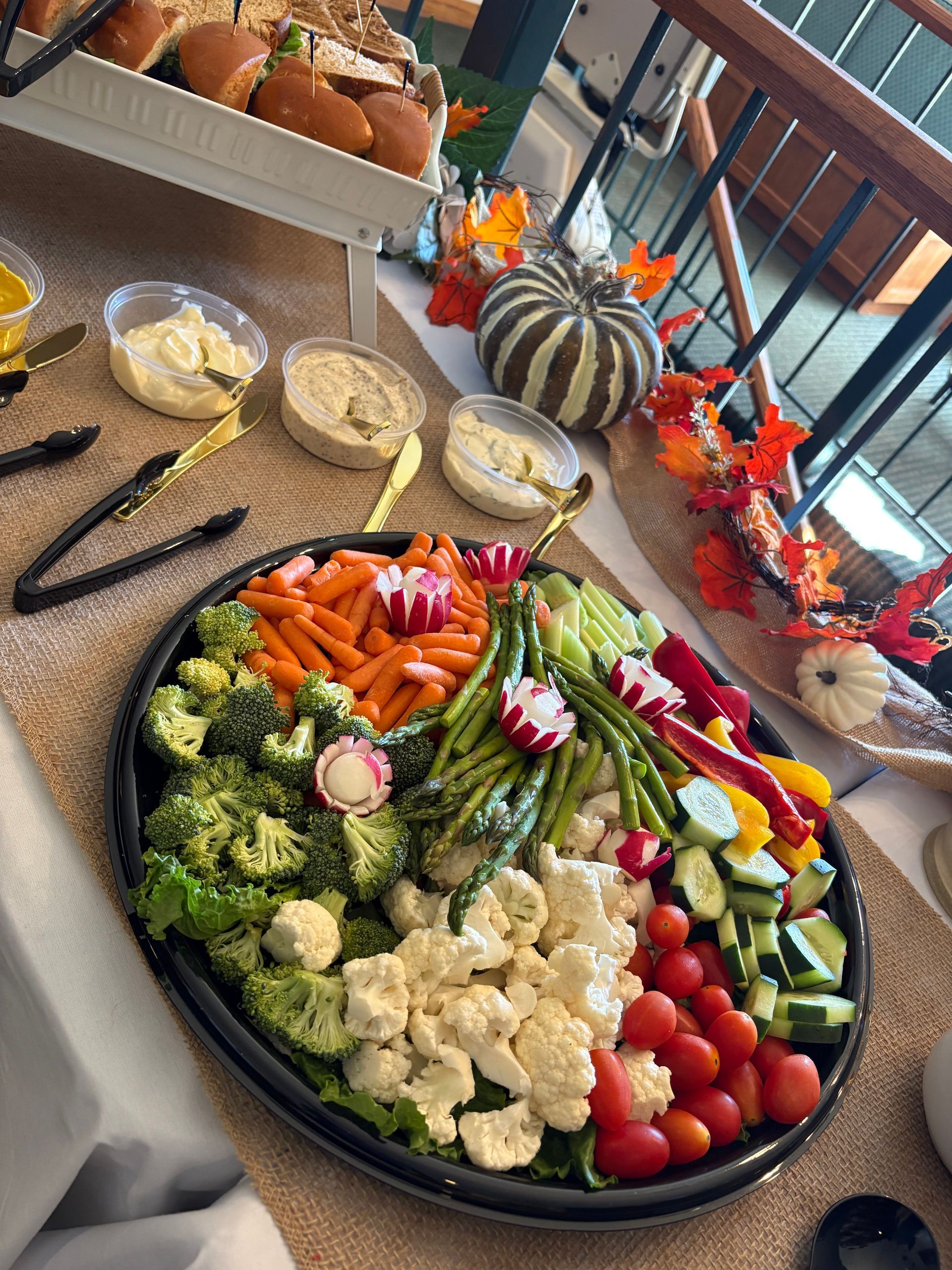 Vegetable platter with dips, sliders, and fall decorations on a buffet table.