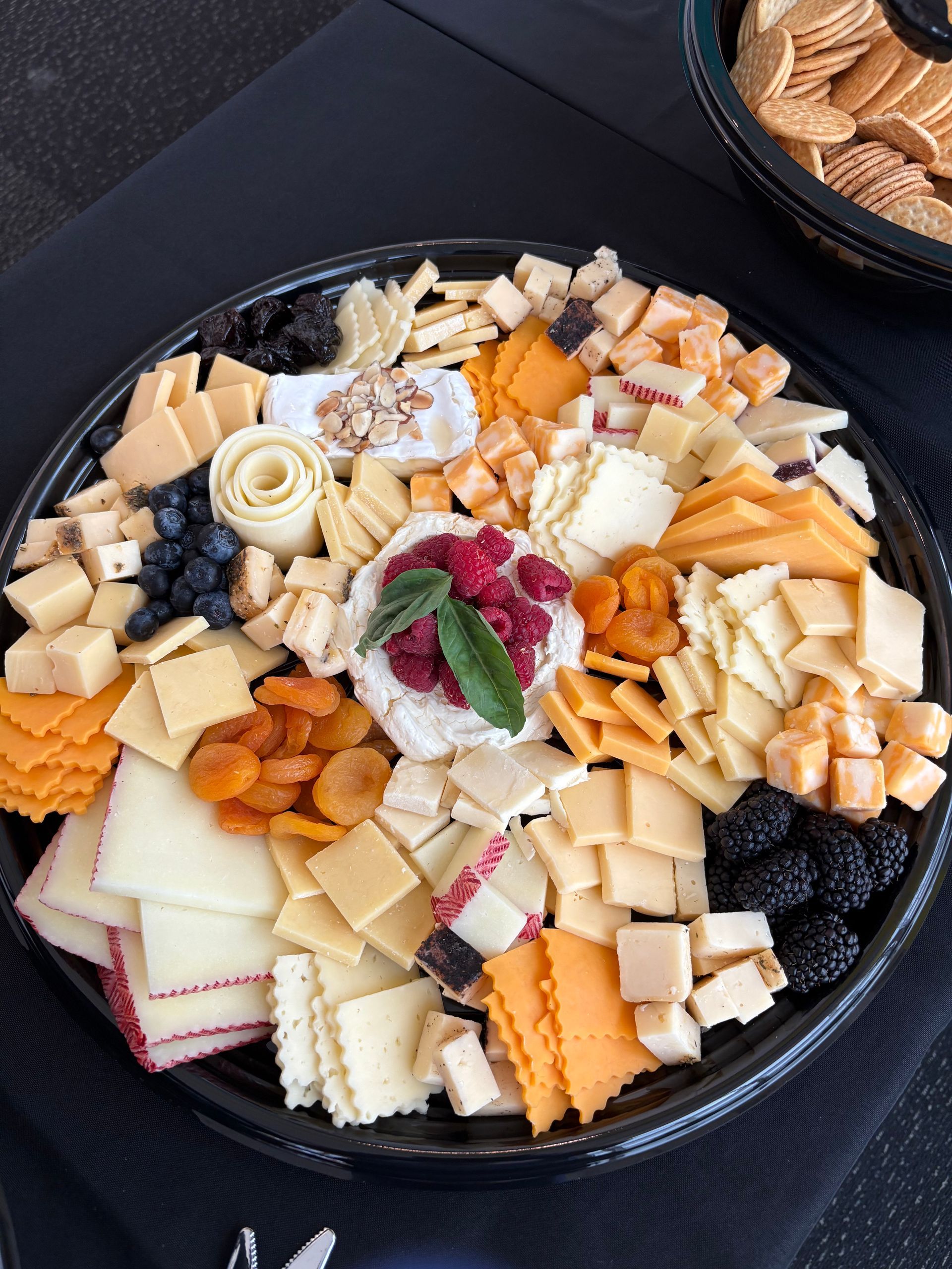 Cheese and fruit platter with a variety of cheeses, dried apricots, berries, and crackers.