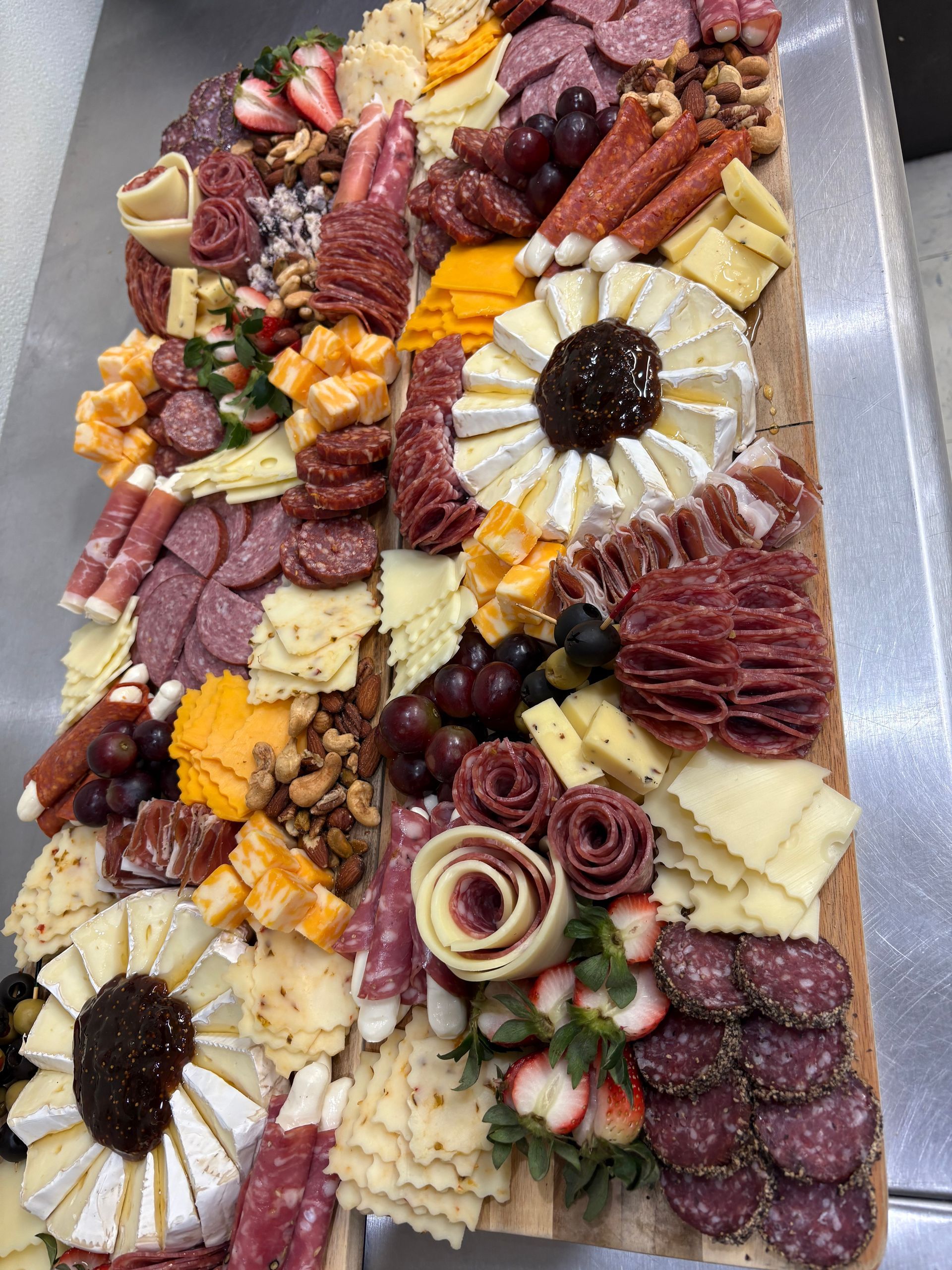 Charcuterie board with cheeses, meats, nuts, fruits. Displayed on a wooden surface.