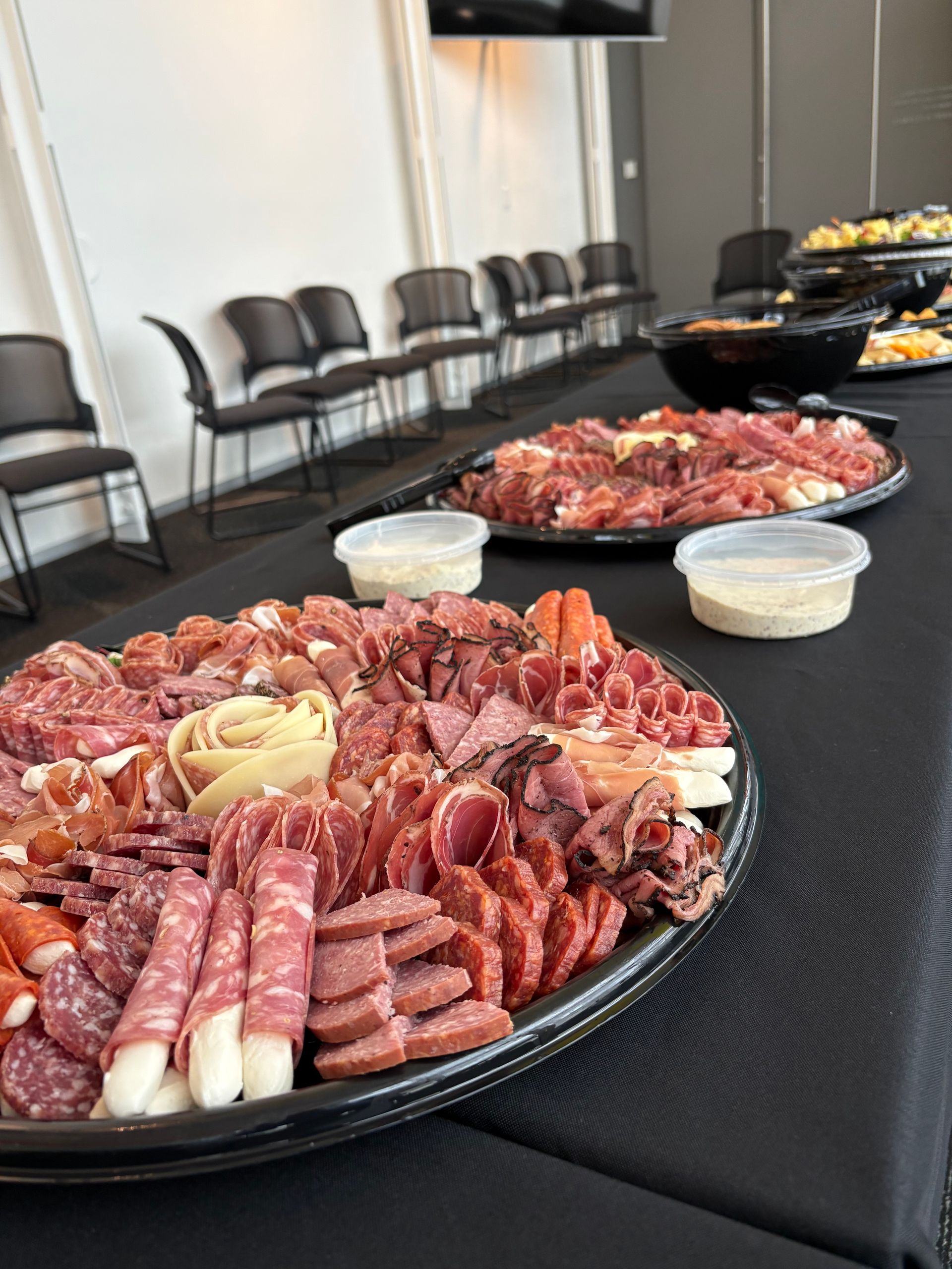 Charcuterie boards with meats and cheeses on a table, with chairs and a black backdrop.