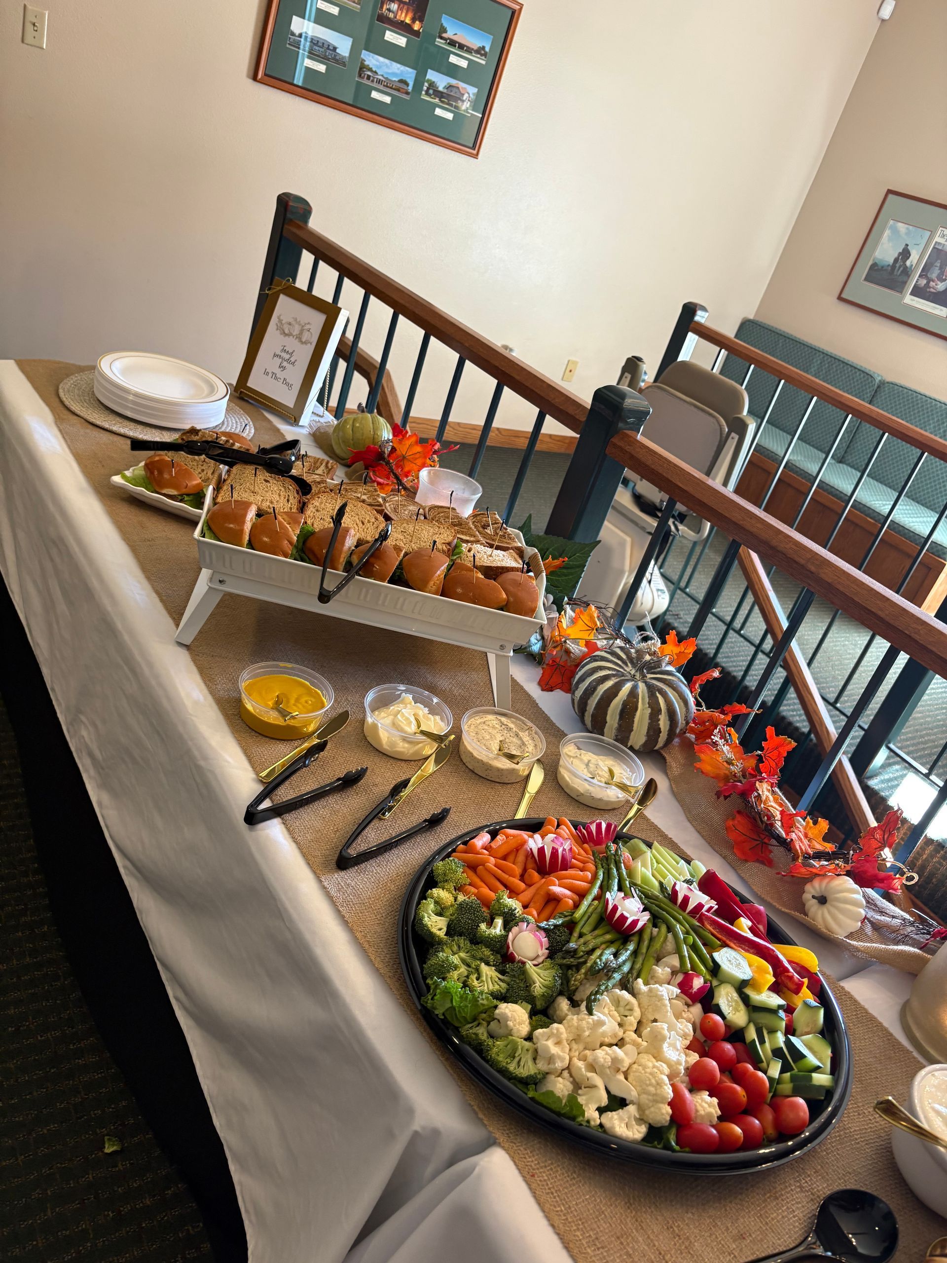 A table displays food: sliced bread, a vegetable tray, dips, and a decorative pumpkin near a staircase.