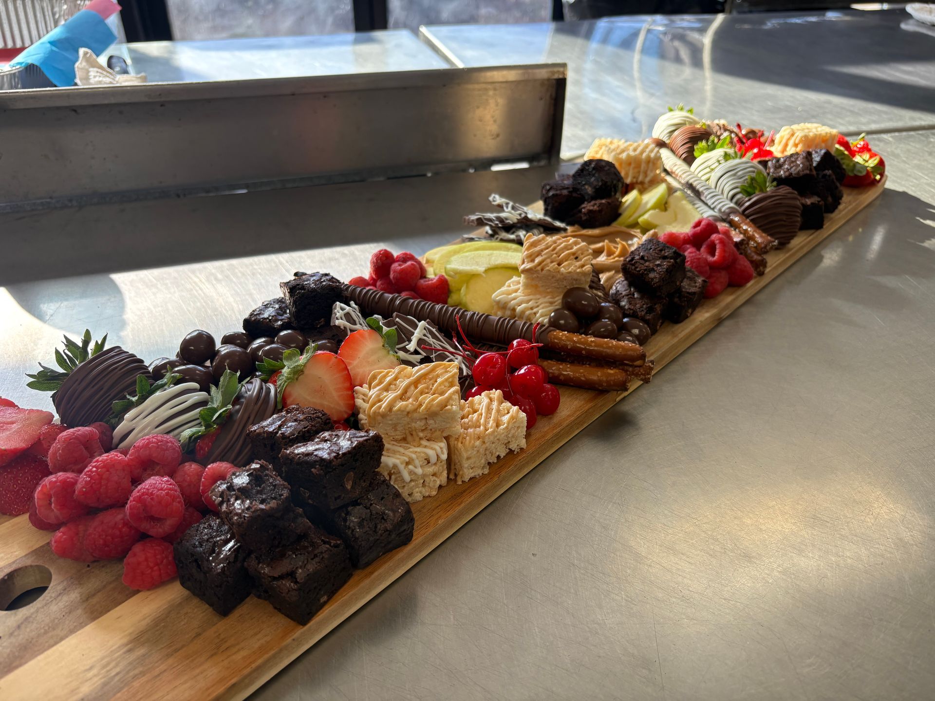 Wooden charcuterie board with assorted desserts, including brownies, berries, and chocolate-covered strawberries.