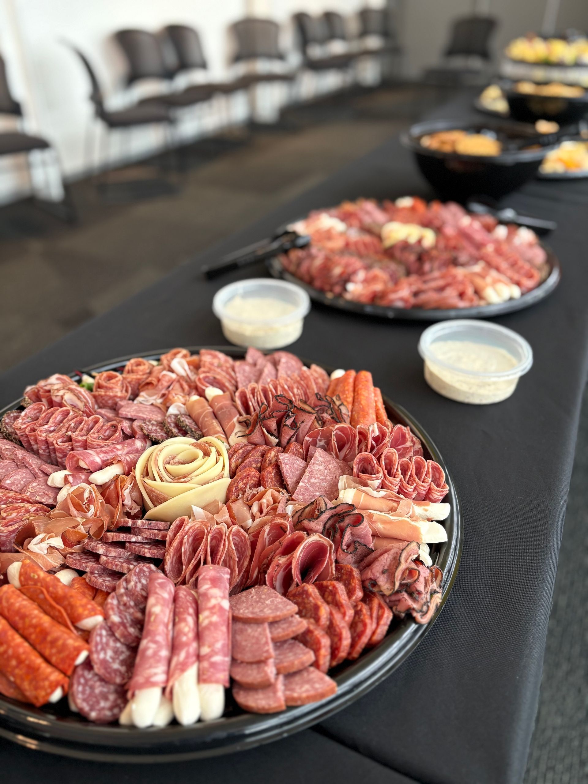 Charcuterie platters on a black table; chairs in the background.