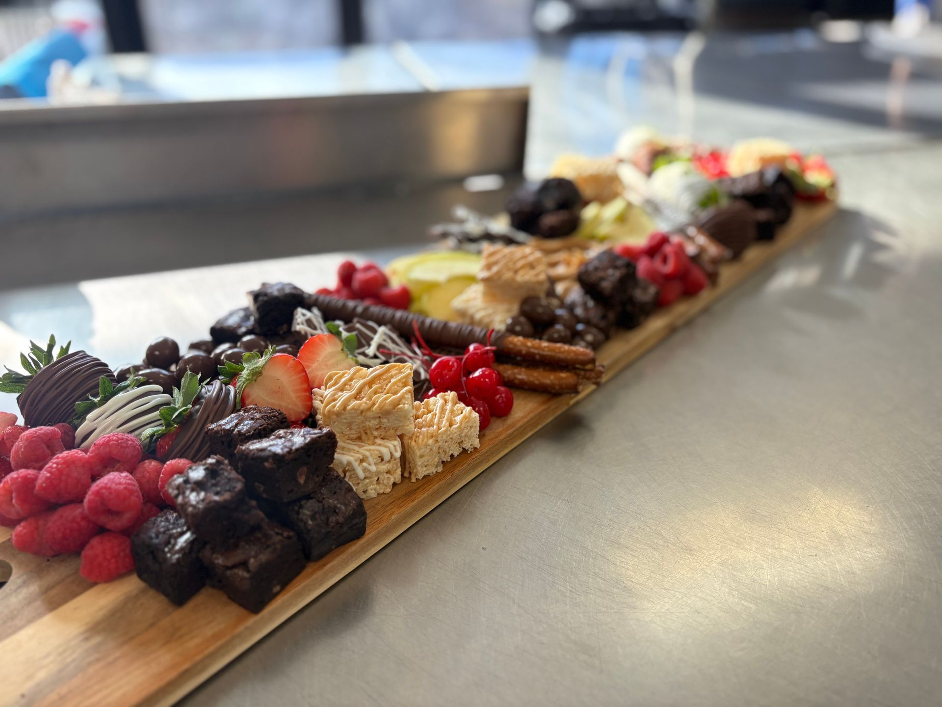 Dessert charcuterie board with brownies, berries, chocolate-covered strawberries, and other sweets on a wooden plank.