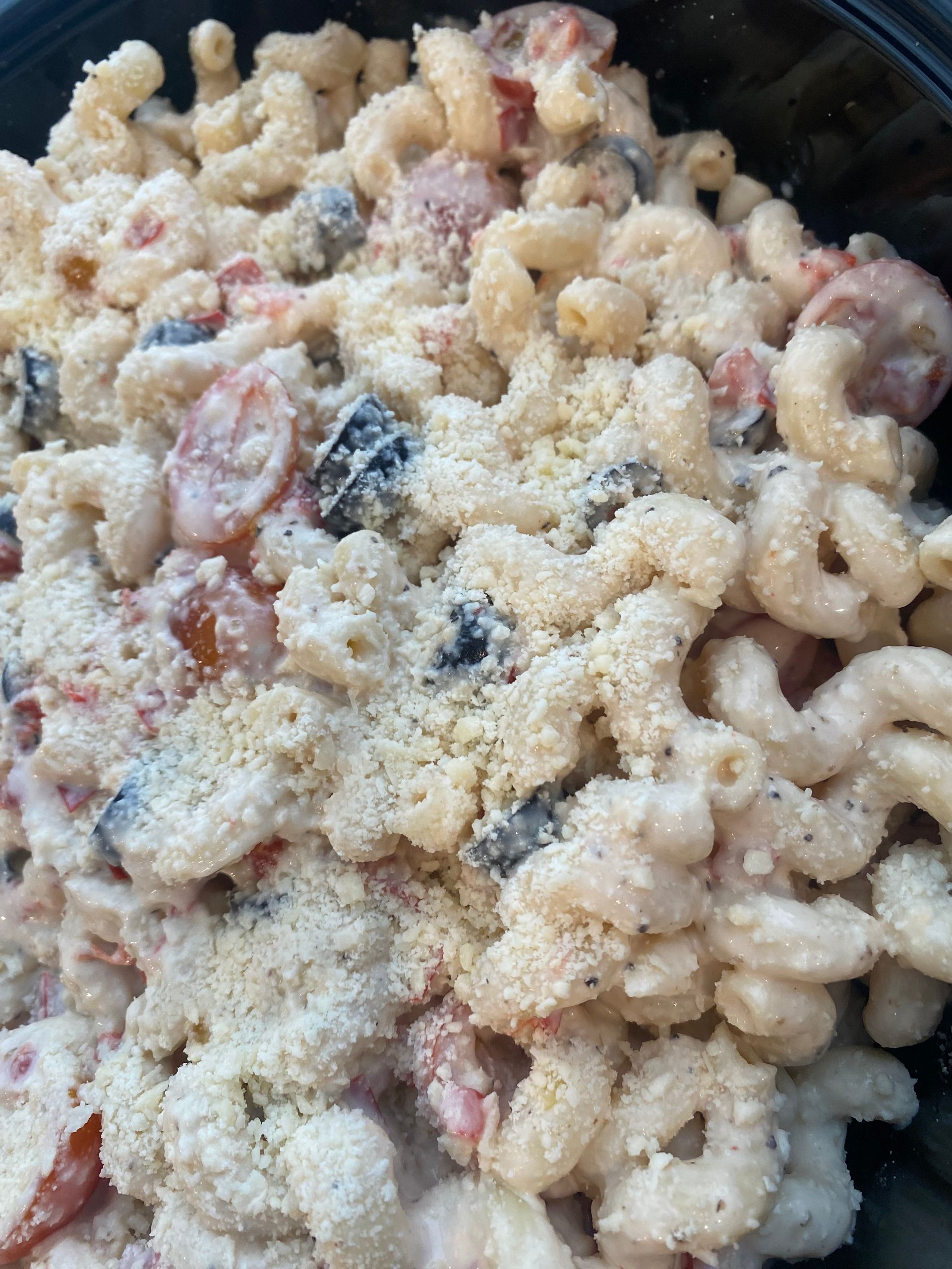 Pasta salad with elbow macaroni, tomatoes, olives, and grated topping.