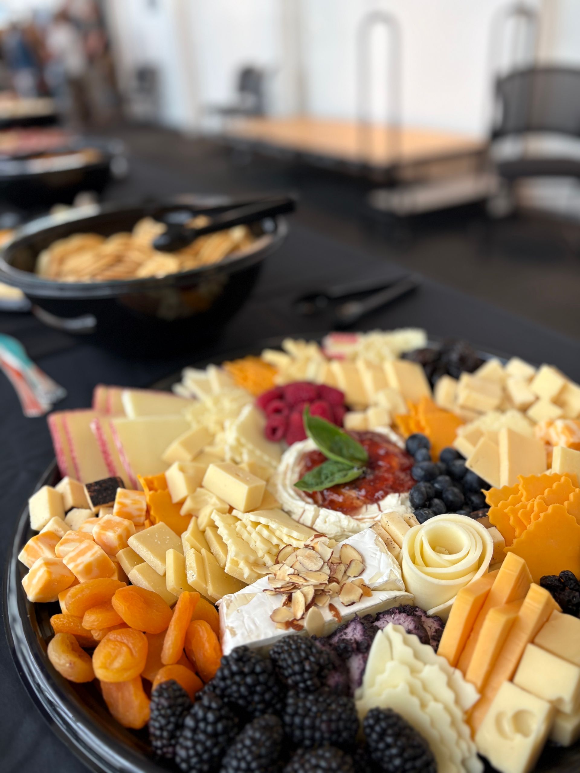 Cheese and fruit platter with crackers in black bowl on a table.