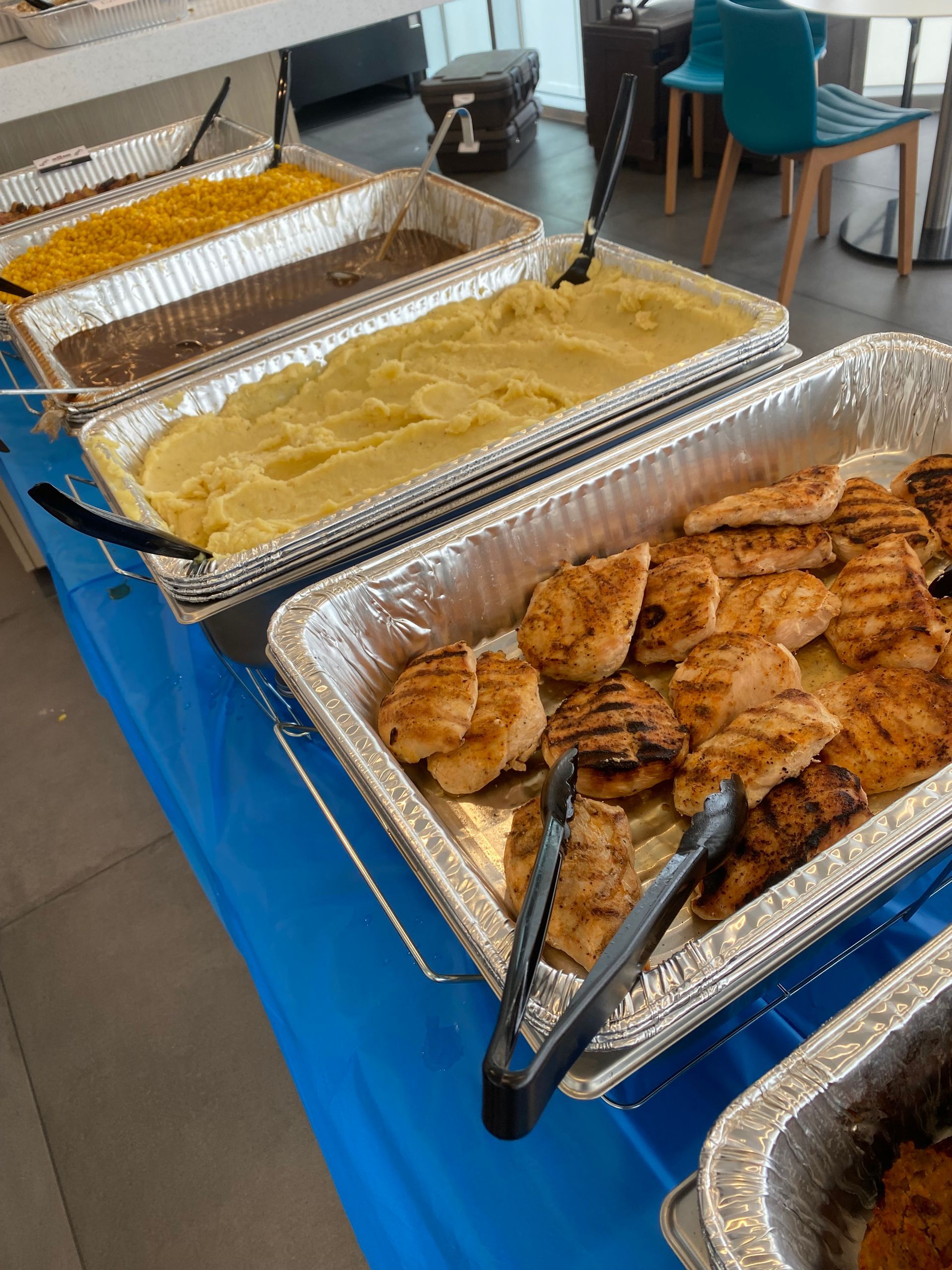 Buffet table with grilled salmon, mashed potatoes, and other dishes. Blue tablecloth.