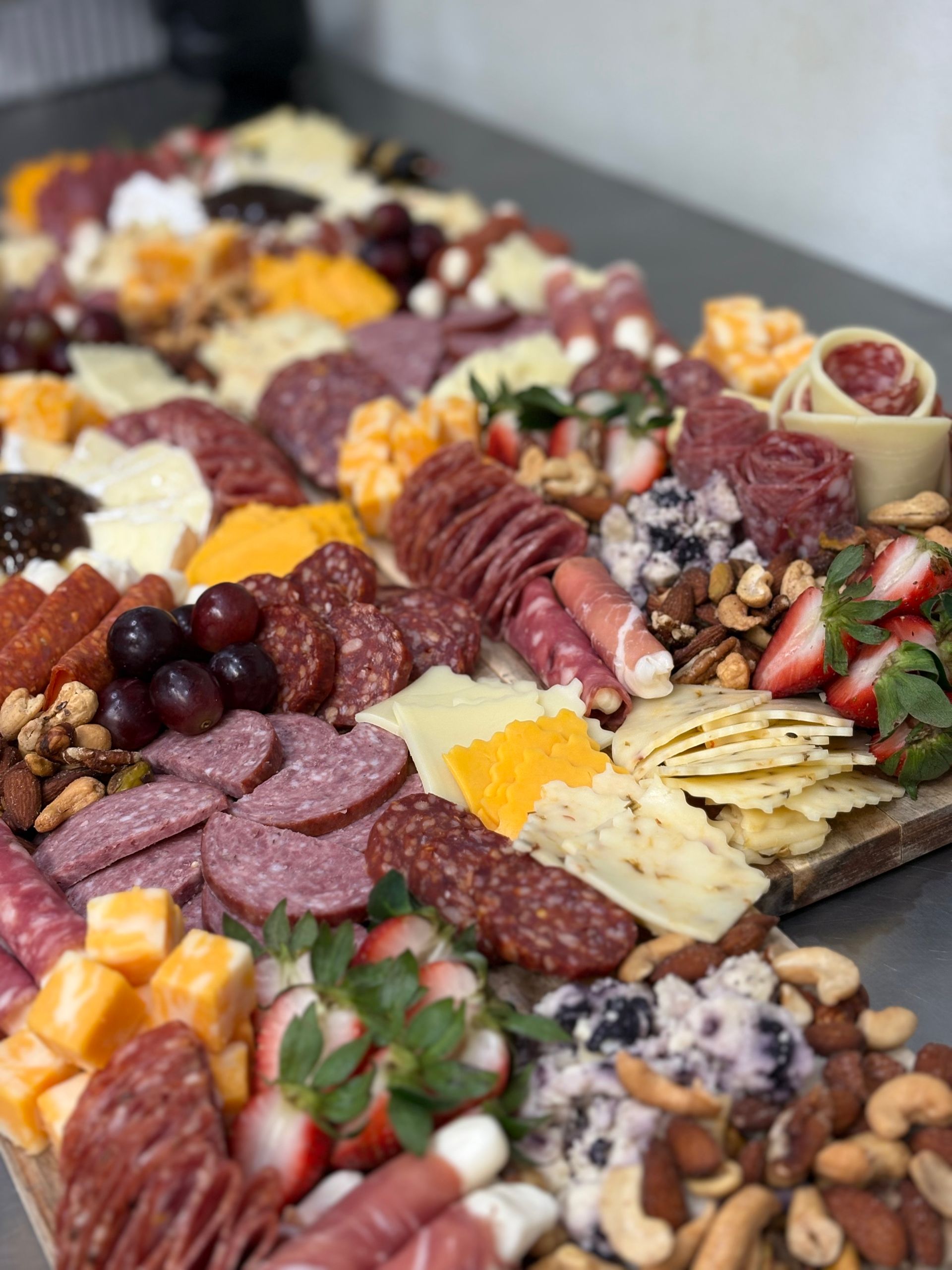 Charcuterie board with cheeses, meats, crackers, berries, and nuts.
