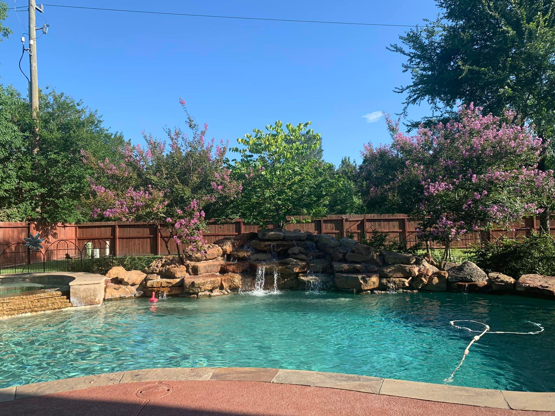 Turquoise resort pool with rock waterfall, pink flowering trees, and two people swimming