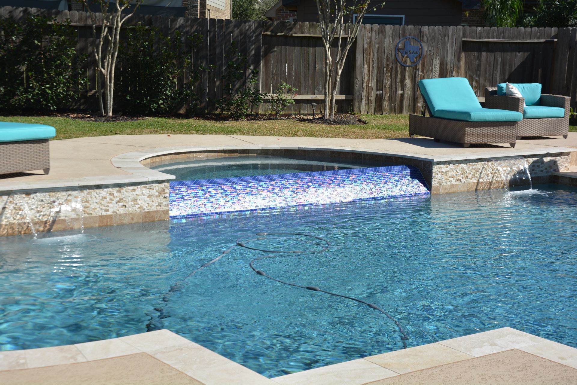 Backyard swimming pool with blue water, stone coping, and turquoise lounge chairs.