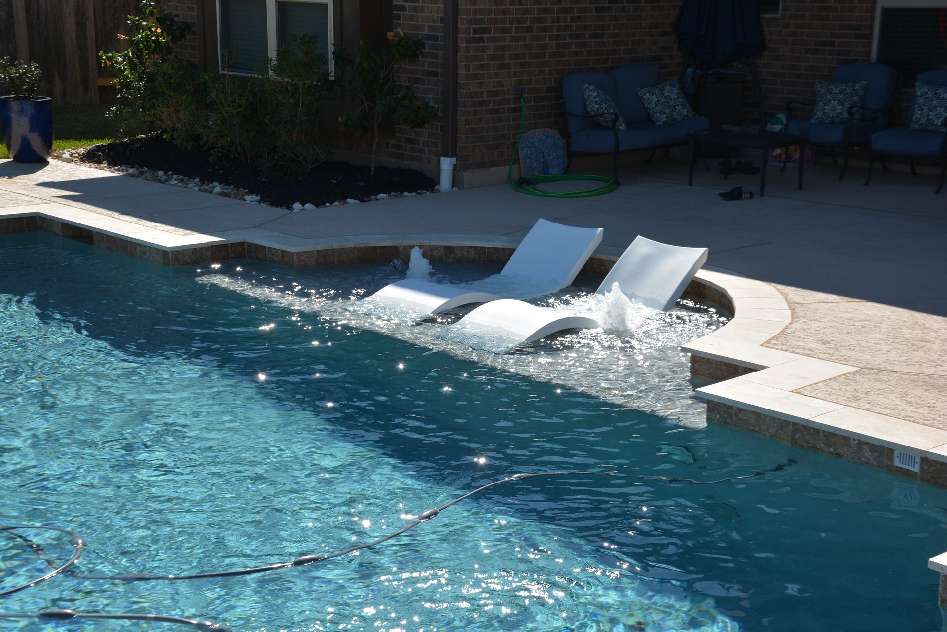 Two white lounge chairs partly submerged in a pool beside a patio