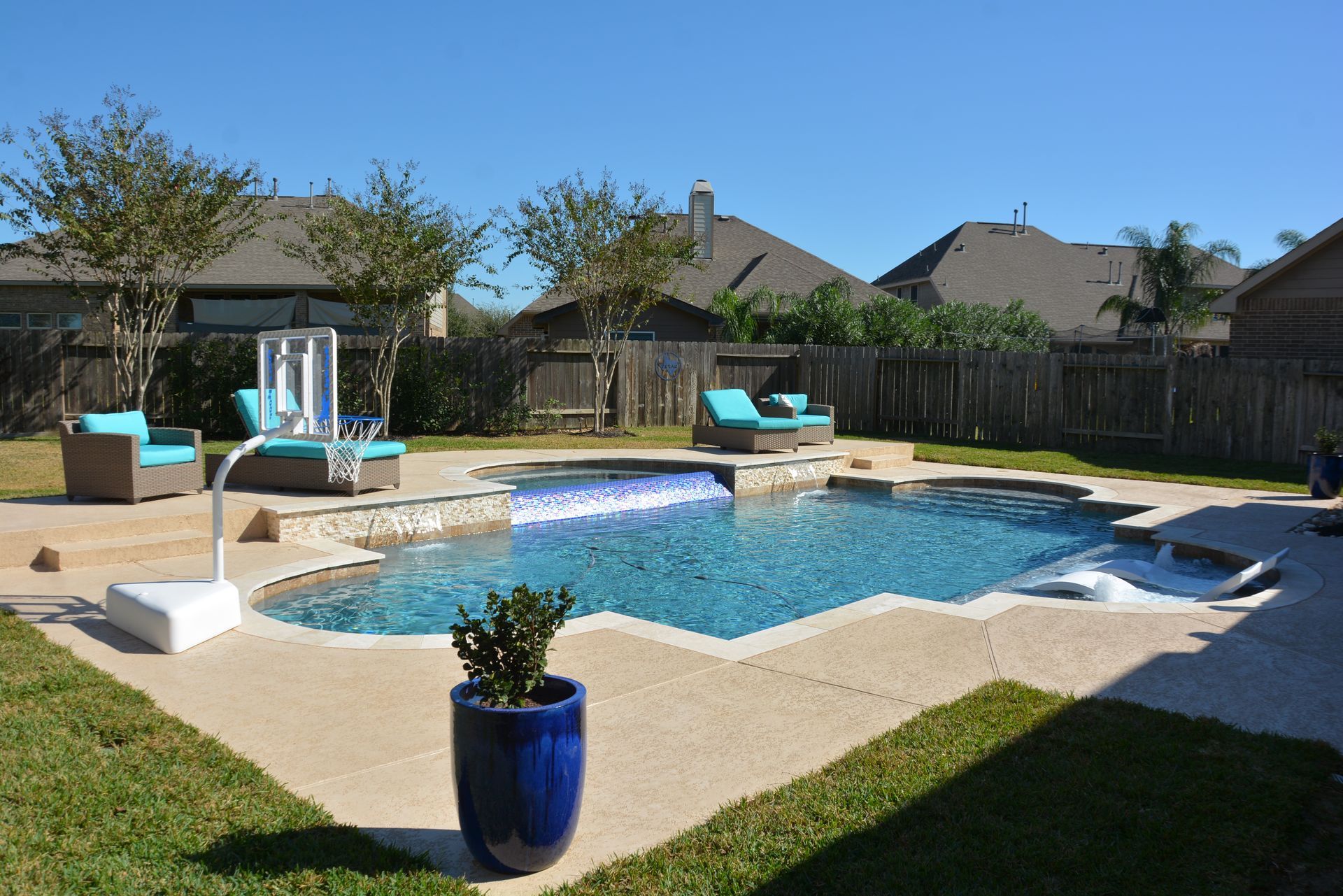 Backyard pool with curved stone deck, blue lounge chairs, and a potted plant in front