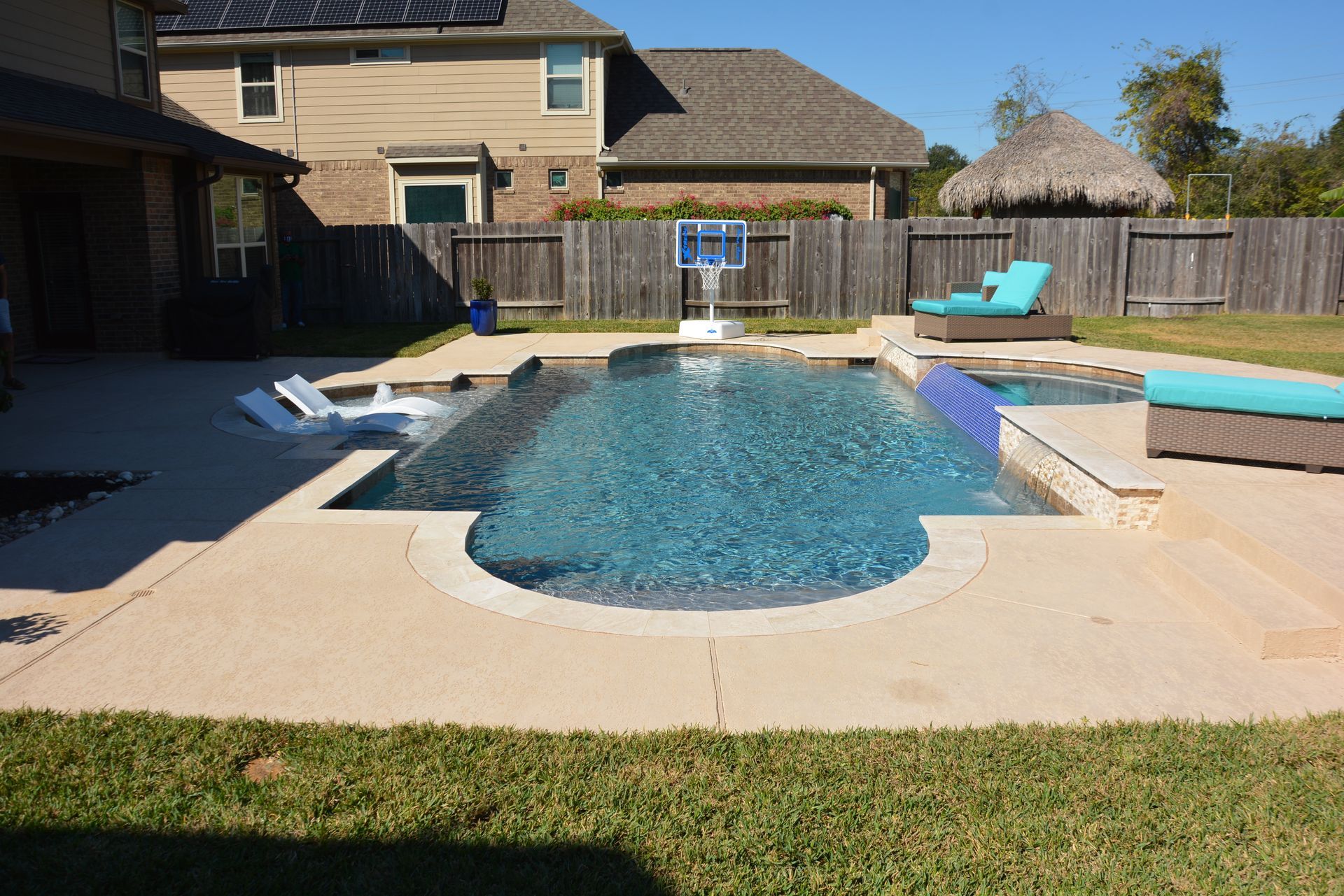 Backyard pool with lounge chairs, a spa, and a two-story house in the background