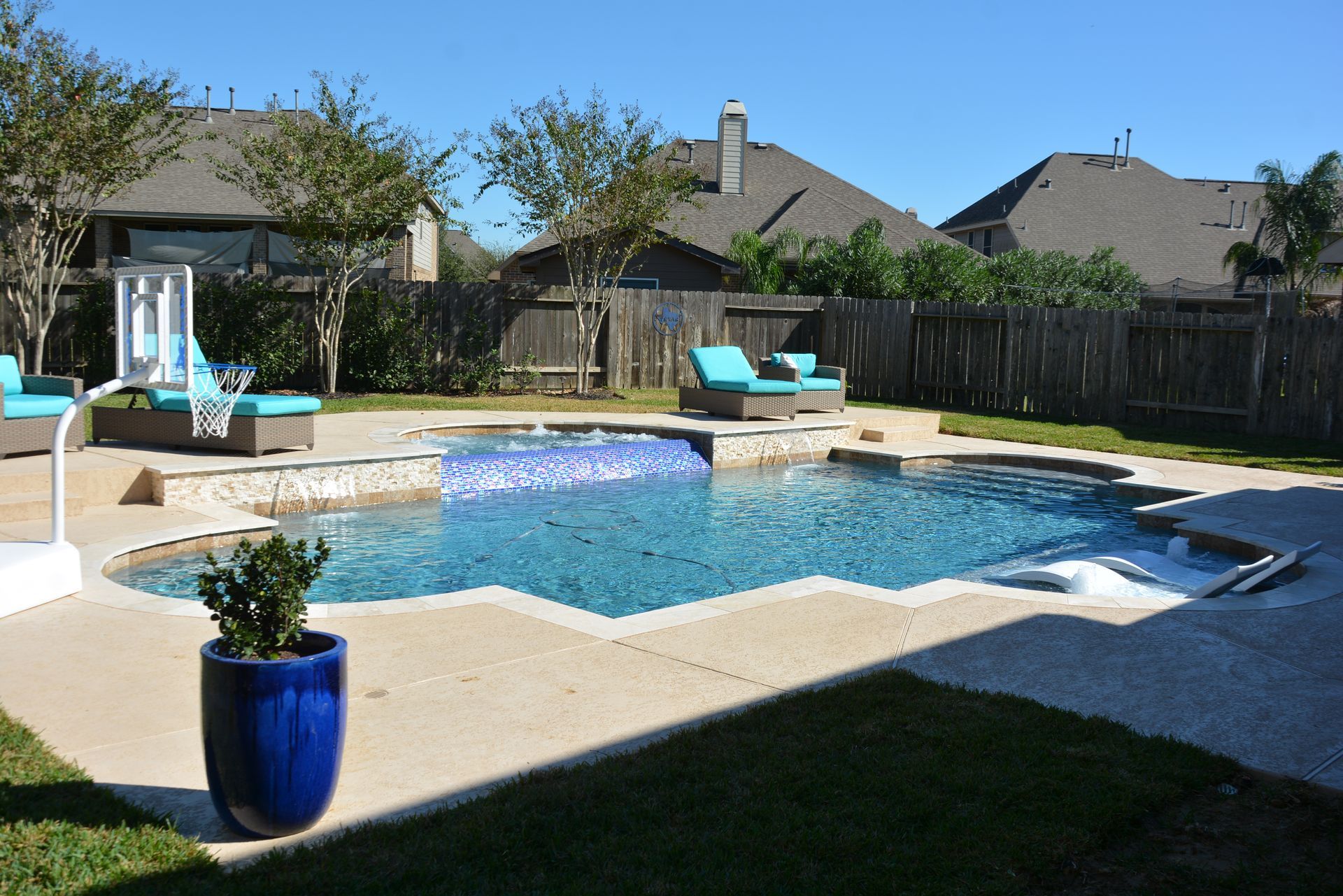 Backyard pool with lounge chairs, a blue planter, and a fenced lawn under clear skies