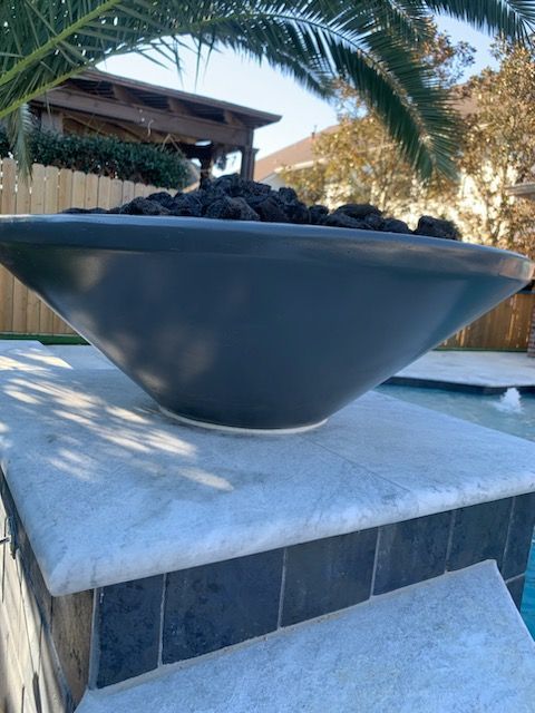 Black decorative bowl on a stone pedestal outdoors in a sunny courtyard garden.