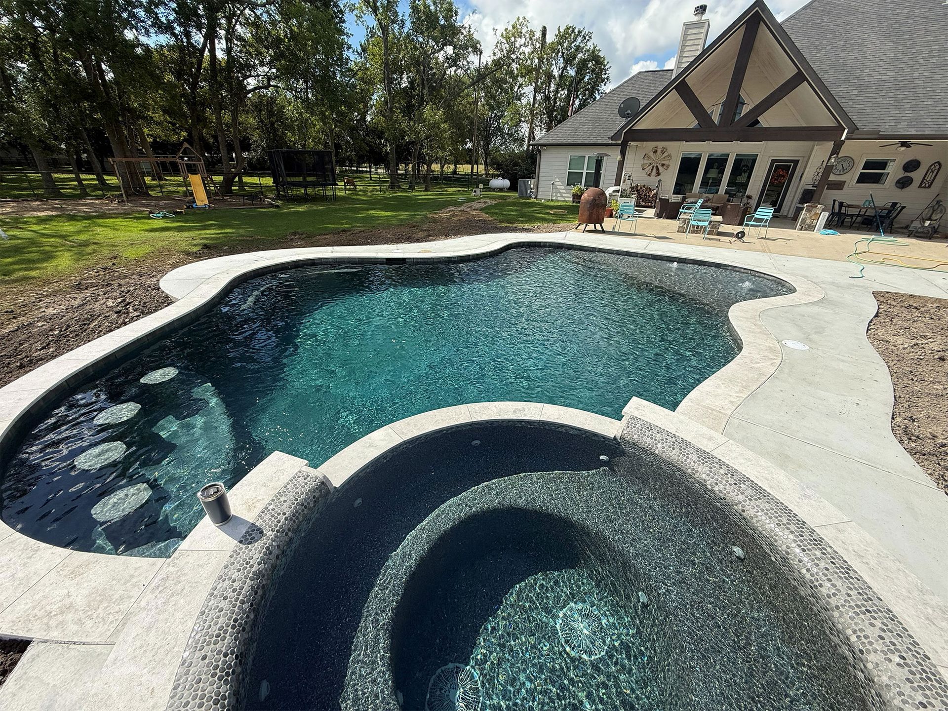 Backyard pool and spa with turquoise water beside a house and patio