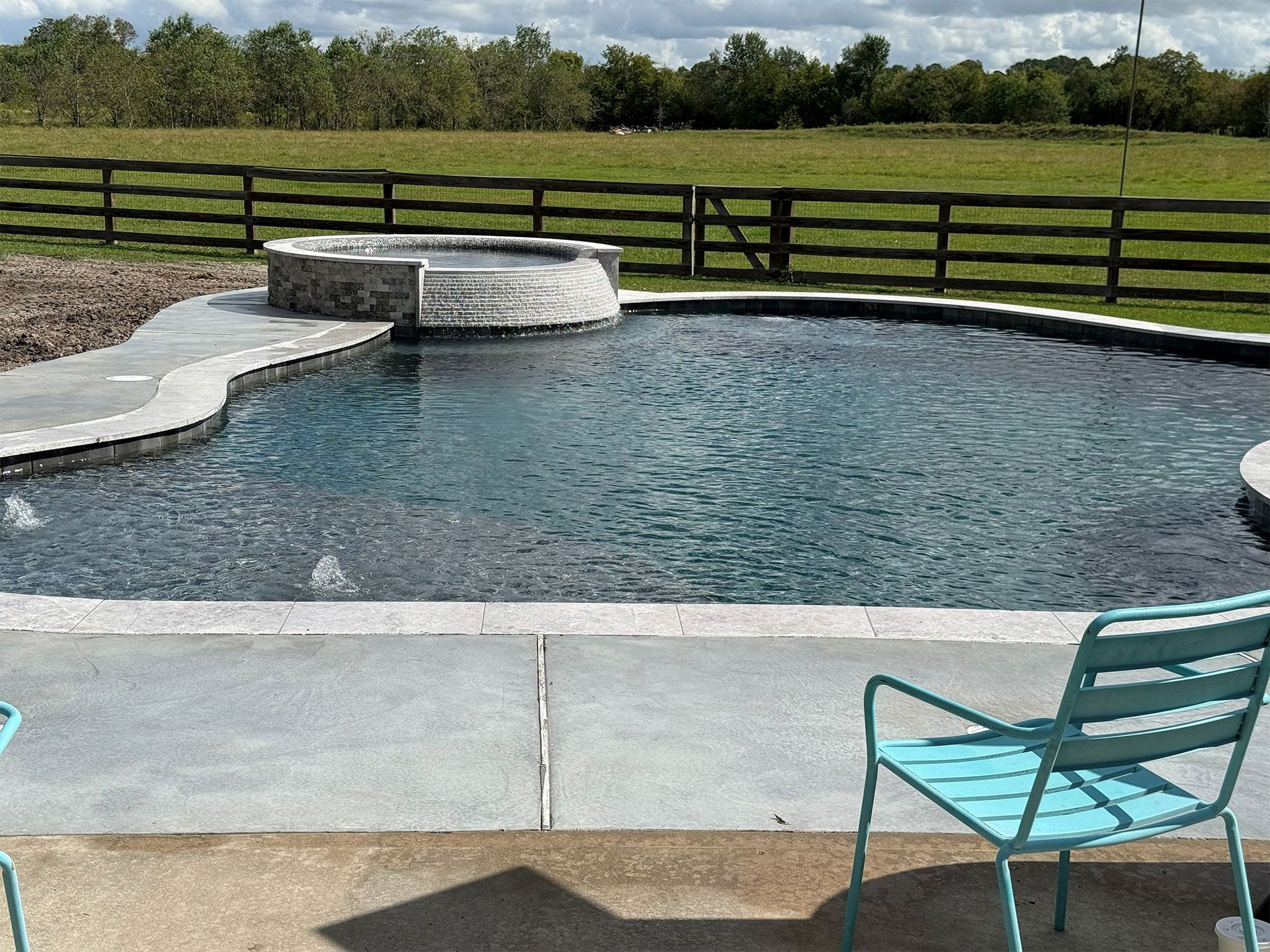 Backyard swimming pool with a turquoise chair, fence, and grassy field beyond